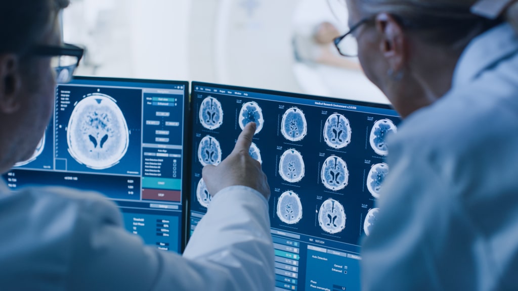 Two people wearing white lab coats pointing to brain imaging on a screen.